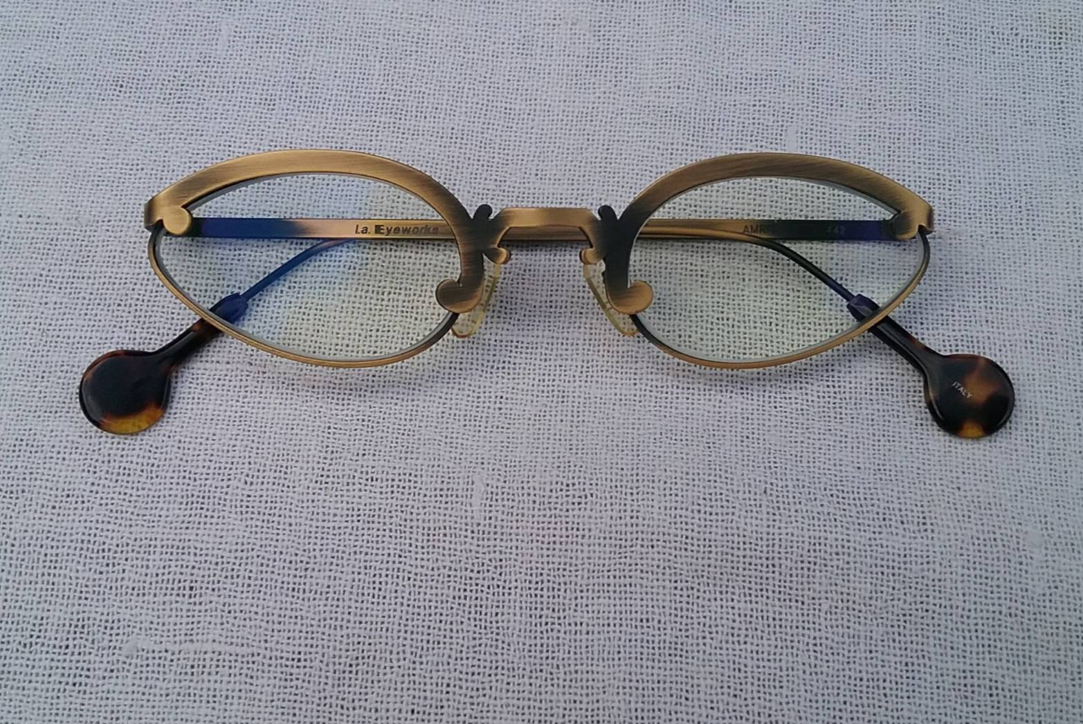แว่นสายตาอเมริกันสตีมพังก์ แอล เอ อายเวิร์ก ทศวรรษ 1990 ผลงานลิมิเต็ดเอดิชันของช่างฝีมือสายพันธุ์แคลิฟอร์เนียน บาร์บารา แมคเรย์โนลด์ และ เก เกราร์ดี  กรอบงานทองรมดำ โบนัสพิเศษ เลนส์บลูโพรเทคมัลติโค้ท ค่าสายตายาวบวก 175 ป้องกันแสงสีฟ้าที่อันตรายได้สมบูรณ์แบบ Vintage L.A. EYEWORKS handcrafted in Italy